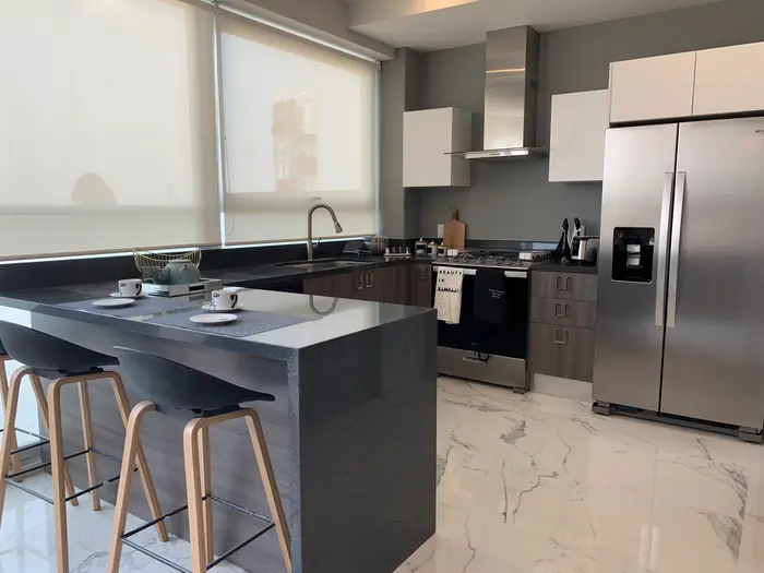 Cocina con barra gris, bancos de madera y refrigerador de acero