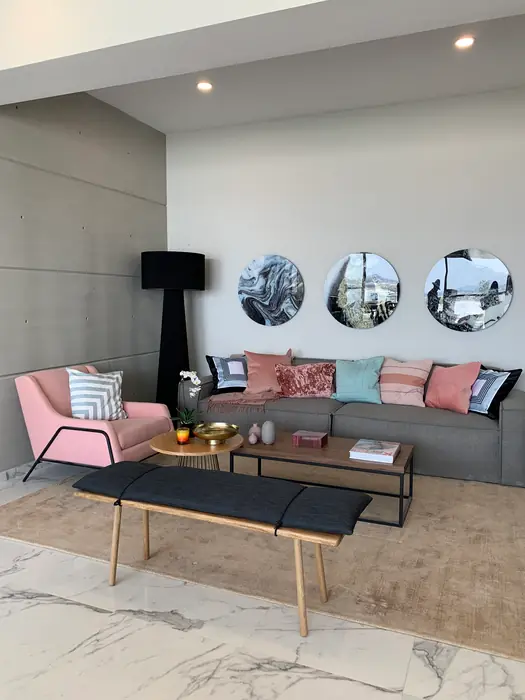 Sala con sillón gris, cojines rosas y espejos circulares