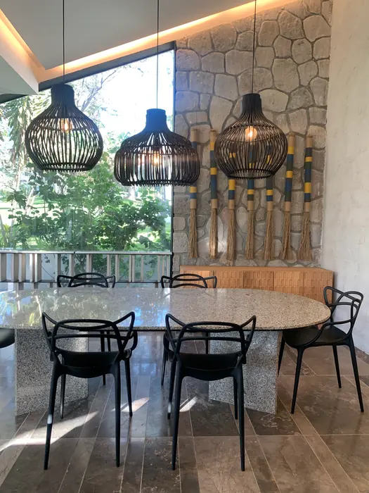 Comedor con lámparas de mimbre y muro de piedra con arte de fibras