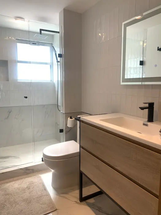 Baño con mueble de madera y regadera de cristal