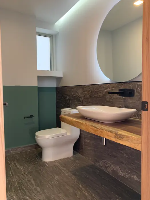 Baño de visitas con lavabo sobre cubierta de madera y muro verde