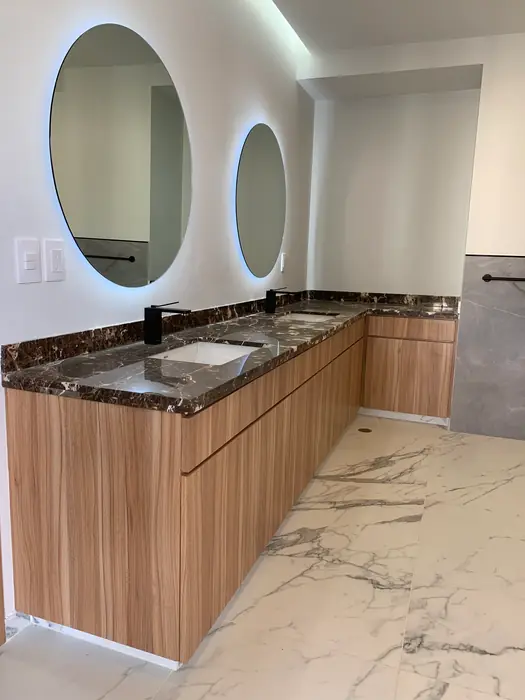 Baño con doble lavabo, espejos redondos iluminados y mueble de madera